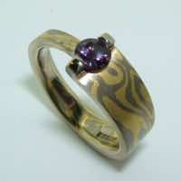 18k white and yellow gold mokume gane tapered band with a purple sapphire in a 18k gold bar setting