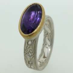 18k white gold and silver mokume gane flat band with small flush set diamonds and an oval amethyst in a 22k gold and silver rub over setting. 