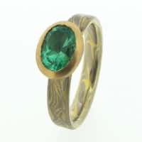 18k white and yellow gold mokume gane flat band with an oval emerald in a 22k yellow gold rub-over setting