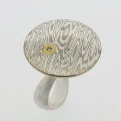 18k white gold and silver mokume gane discus with 22k gold detail and diamond presented on a sterling silver curved band.