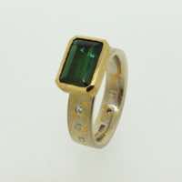 Platinum and 22k gold mokume gane 5mm flat band with flush set diamonds and an emerald-cut green tourmaline in a 22k gold pod setting. 