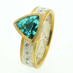 18k white gold and silver mokume gane flat band with 22k gold rails and  flush set diamonds and a trillion cut Paraiba tourmaline in a 22k gold rub-over pod setting.