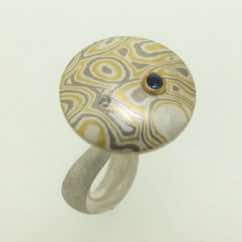 22k gold, 18k white gold and silver mokume gane discus with blue sapphire and diamonds presented on a sterling silver curved band.