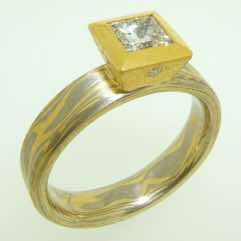 18k white and yellow gold mokume gane 4mm flat band with a princess cut diamond in a 22k gold box setting (setting has a small flush set diamond on each face).